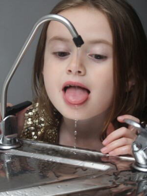 A well shot photo of a little girl trying to drink out of a tap.