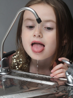 A well shot photo of a little girl trying to drink out of a tap.