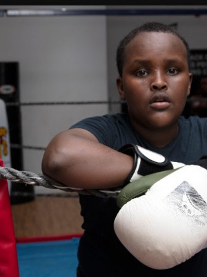 An image of a boy leaning on the ropes in a boxing ring.