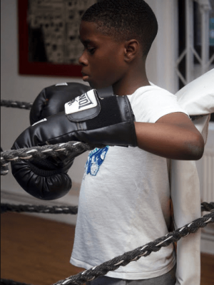 A well shot photo of a boy in a boxing ring resting in the corner.