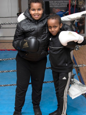 A well shot photo of two boys in a boxing ring embracing one another.