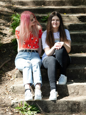 A well shot photo of a two sisters sitting with each other on some steps.