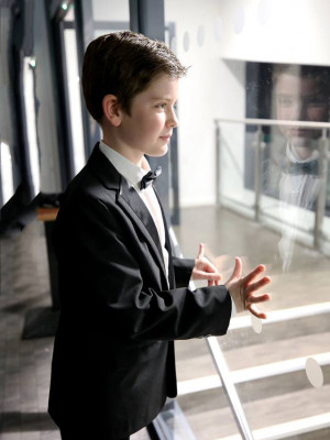 An image of a boy in a tuxedo leaning on a glass window.
